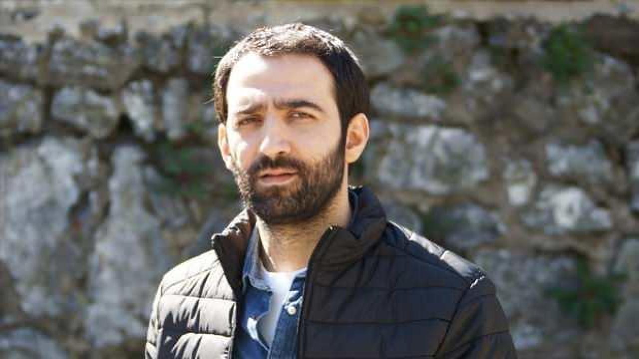 Ferit Kaya, siyah mont giymiş halde taş duvar önünde çekilmiş portre fotoğrafı. Bakışlarındaki derinlik ve karakteristik sakalıyla dikkat çekiyor, rol aldığı bir projeden tanıtım fotoğrafı olabilir.