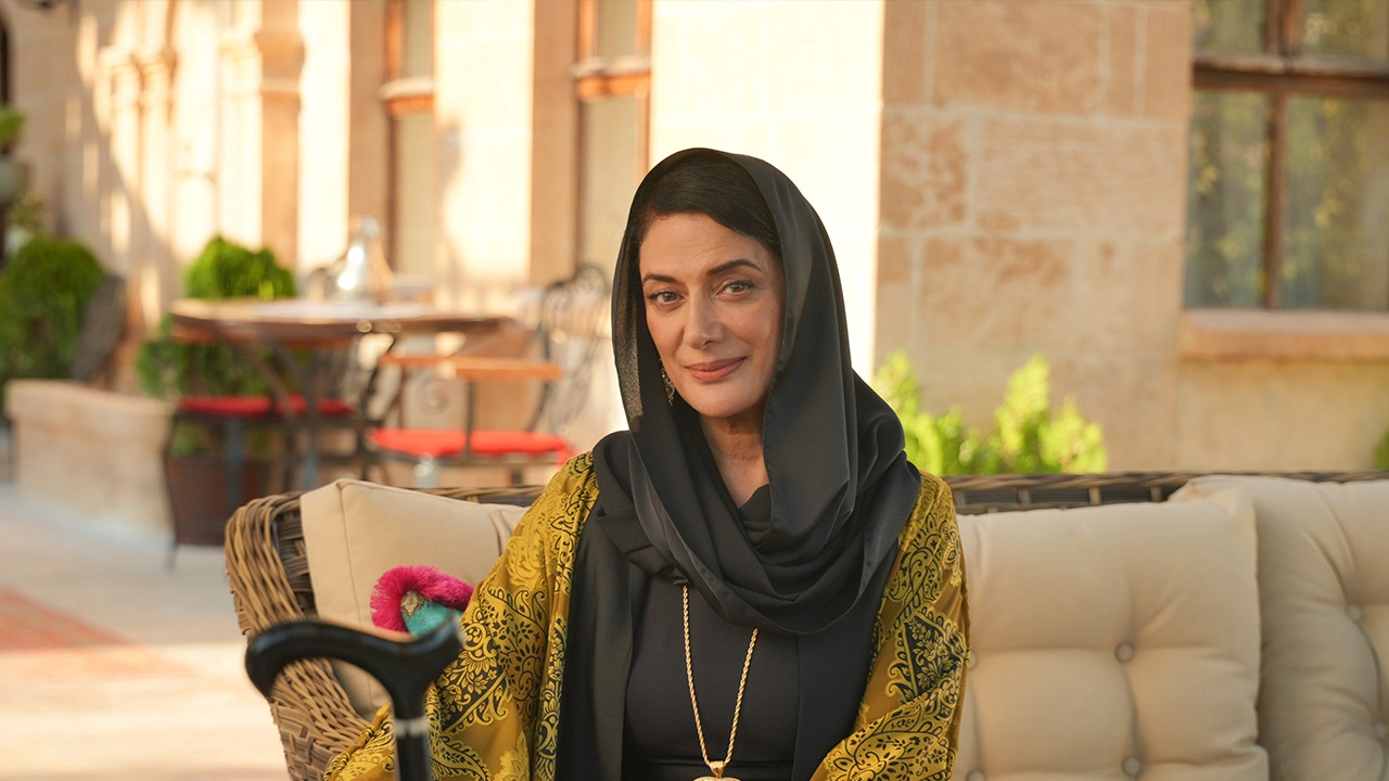 Veda Yurtsever, Halef: Köklerin Çağrısı dizisinde güçlü ve sakin duruşuyla karakterini yansıtırken, açık havada otururken görülüyor.